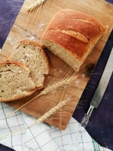 Sliced whole wheat bread on a wooden board with wheat stalks and a knife, perfect for baking and food photography.